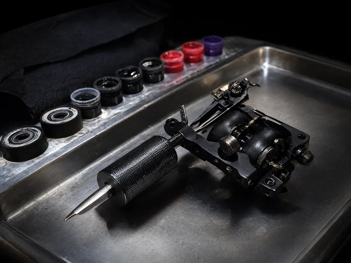 A black rotary tattoo machine beside caps of black, red and violet ink on a steel tray